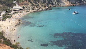A coastal area with a beach, rocky cliffs, and a boat in the water. - Oceanfront Retreat in Sant Josep de sa Talaia With Shared Pool (Sant Josep de sa Talaia)