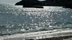 A beach with a rocky cliff and a boat in the water. - Oceanfront Retreat in Sant Josep de sa Talaia With Shared Pool (Sant Josep de sa Talaia)