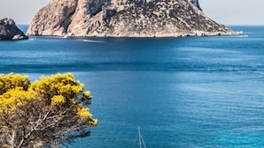 A clear view of a rocky island with a sailboat in the water. - Oceanfront Retreat in Sant Josep de sa Talaia With Shared Pool (Sant Josep de sa Talaia)