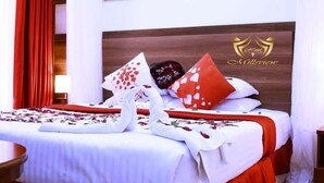 A hotel room with a neatly made bed, red curtains, and a wooden headboard with the hotel logo. - Millsview hotel (Kisumu)