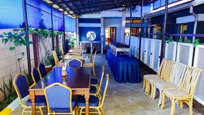 A covered outdoor dining area with a long table and chairs, surrounded by potted plants and a row of air conditioning units. - Millsview hotel (Kisumu)