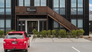 Un bâtiment moderne, sur lequel on peut lire l’enseigne « 12th Avenue Suites », avec un escalier et une voiture rouge garée devant.