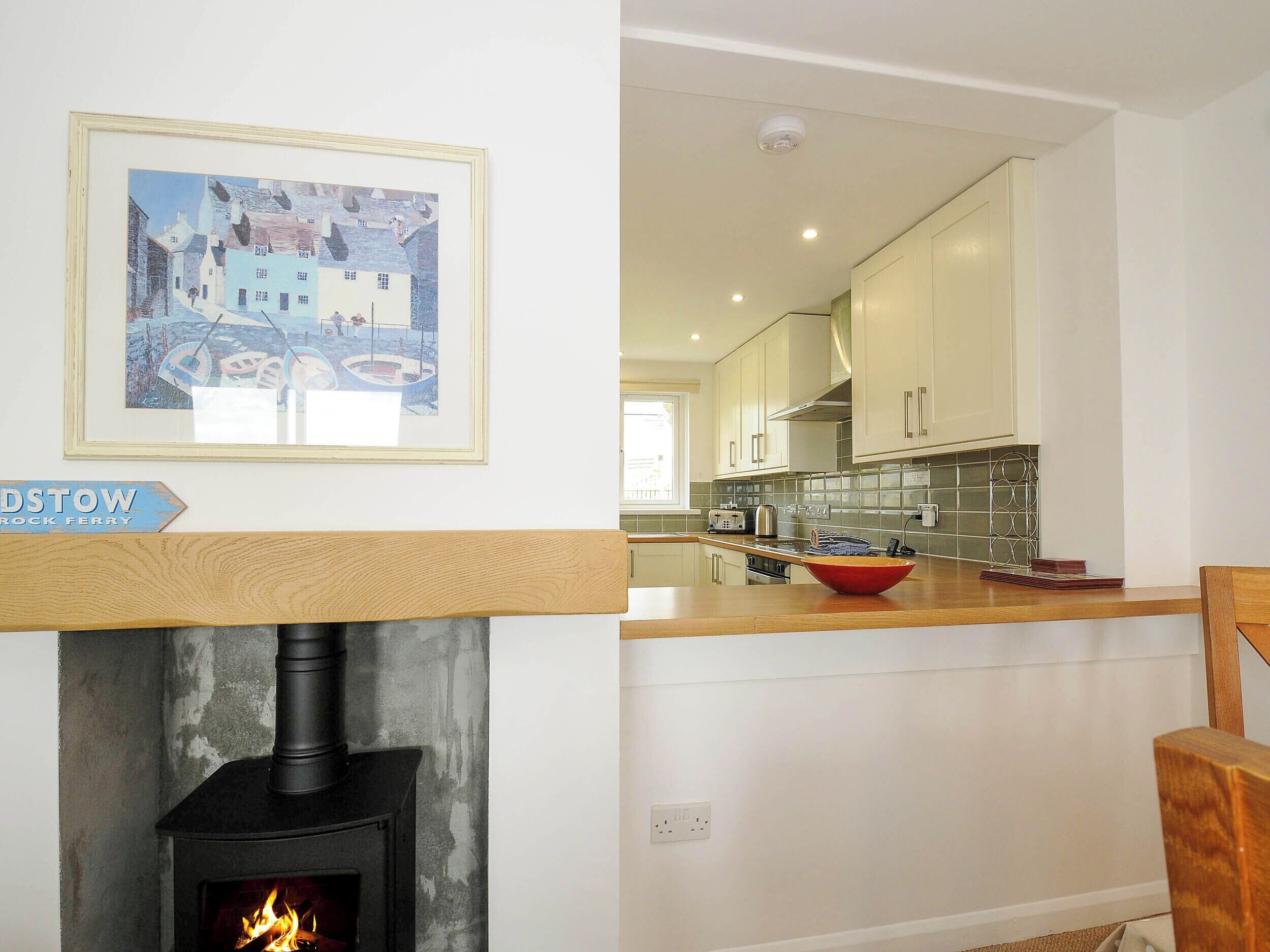 A modern kitchen with white cabinets, a wooden countertop, and a stone fireplace.