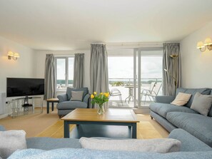 A modern living room with a flat-screen TV, grey sofas, a wooden coffee table, and a view of the sea through large windows. - Slipway 14 (Wadebridge)