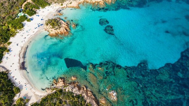 An aerial view of a beach with clear turquoise waters, rocky outcrops, and a sandy shoreline. - Charming House in Sassari With Ocean Views (Arzachena)