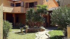A two-story building with a tiled roof, a stone staircase, and a garden with various plants. - Charming House in Sassari With Ocean Views (Arzachena)