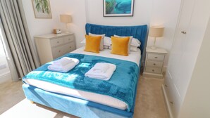 Un letto rifatto con cura, con lenzuola e copriletto blu e bianchi, due cuscini gialli e due asciugamani bianchi piegati.