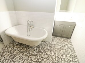 A bathroom with a freestanding bathtub, a showerhead, and a patterned floor. - Valley View (Leyburn)