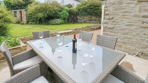 A glass-top table with wicker chairs, a bottle of wine, and wine glasses, set against a stone wall. - Valley View (Leyburn)