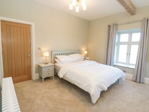 A bedroom with a bed, two bedside tables with lamps, a wooden door, a window with curtains, and a radiator. - Valley View (Leyburn)