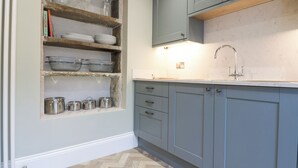A kitchen with wooden shelves holding dishes and cookware, a sink, and cabinets. - Valley View (Leyburn)