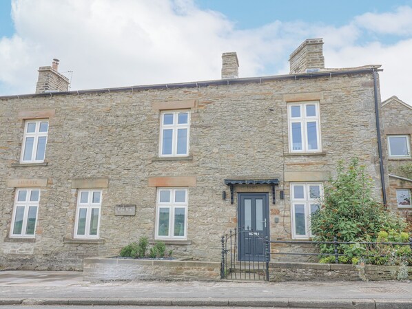 A stone building with multiple windows and a black door, featuring a plaque with the year 1905. - Valley View (Leyburn)