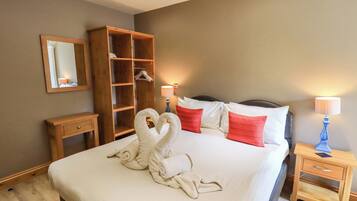 A hotel room with a large bed, a wooden wardrobe, a bedside table with a lamp, and a mirror on the wall.