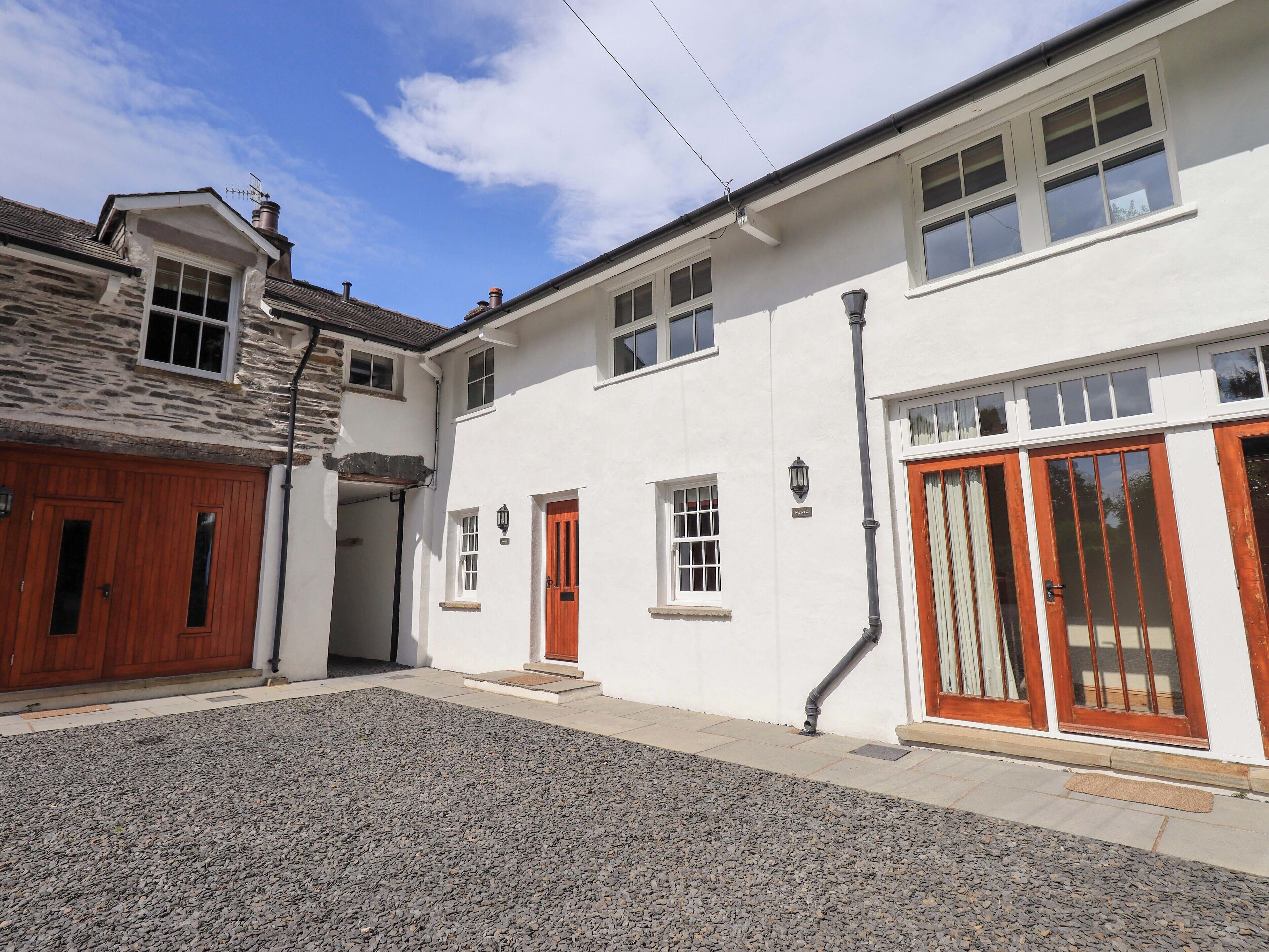 A two-story building with a stone facade, a gravel driveway, and a red door.