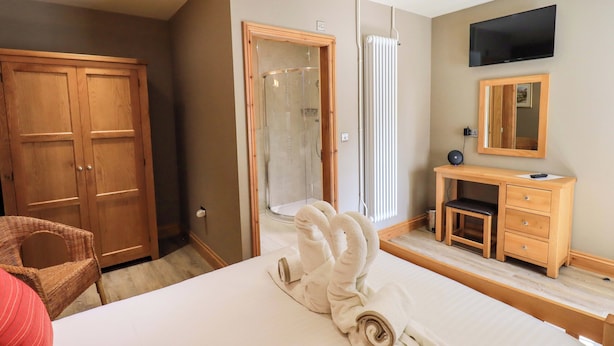 Habitación de hotel con cama, armario de madera, baño con ducha, escritorio con silla y televisor montado en la pared.