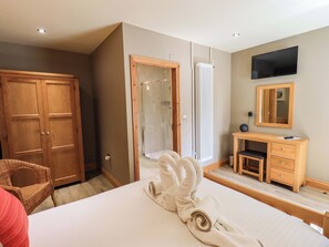 Habitación de hotel con cama, armario de madera, baño con ducha, escritorio con silla y televisor montado en la pared.