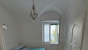 A bedroom with a bed, a window, a chandelier, and patterned floor tiles. - Heartbreaking sea View House in Capri - Italy (Capri)