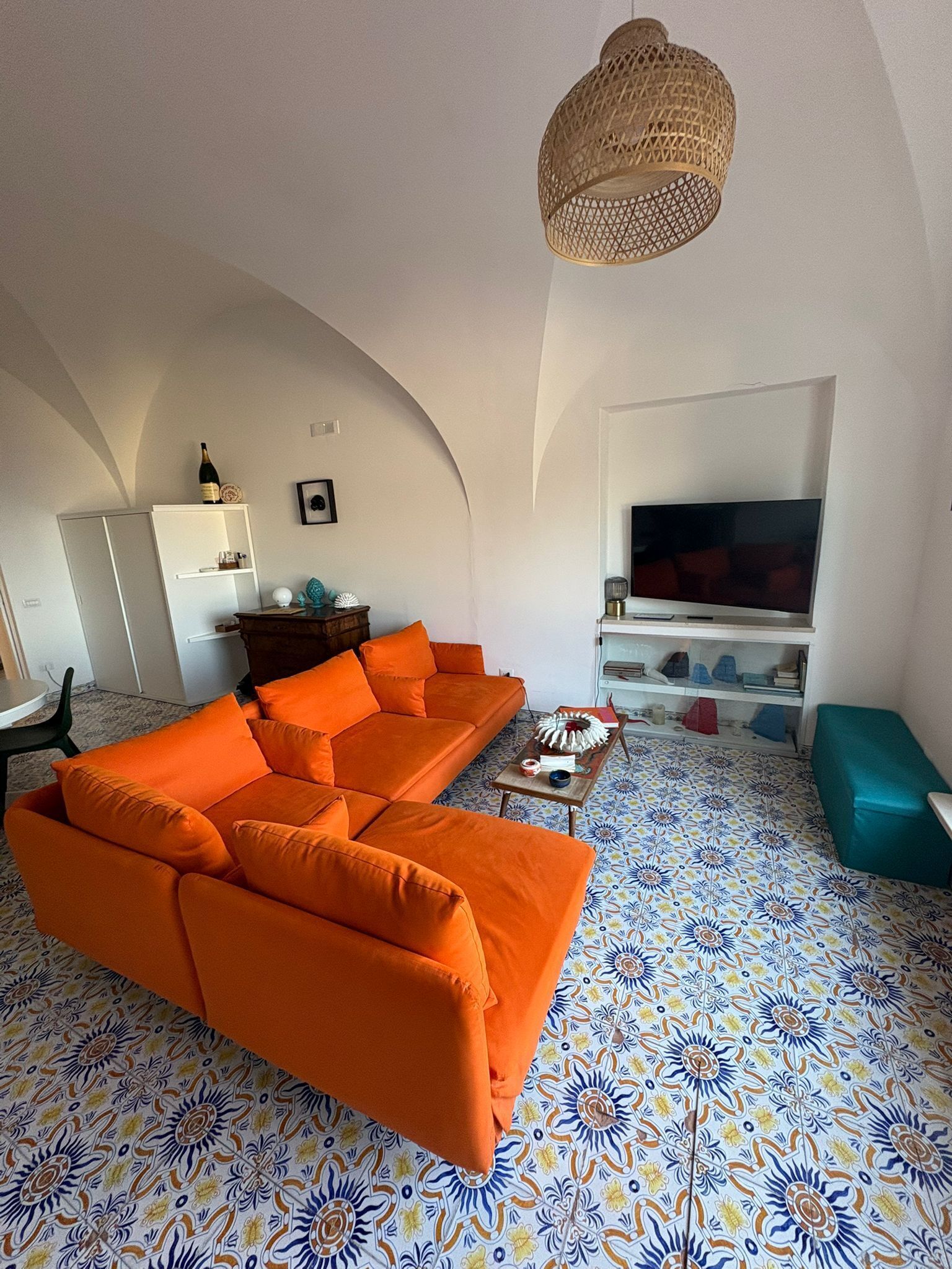 A living room with a large orange sofa, a television, and a patterned floor.