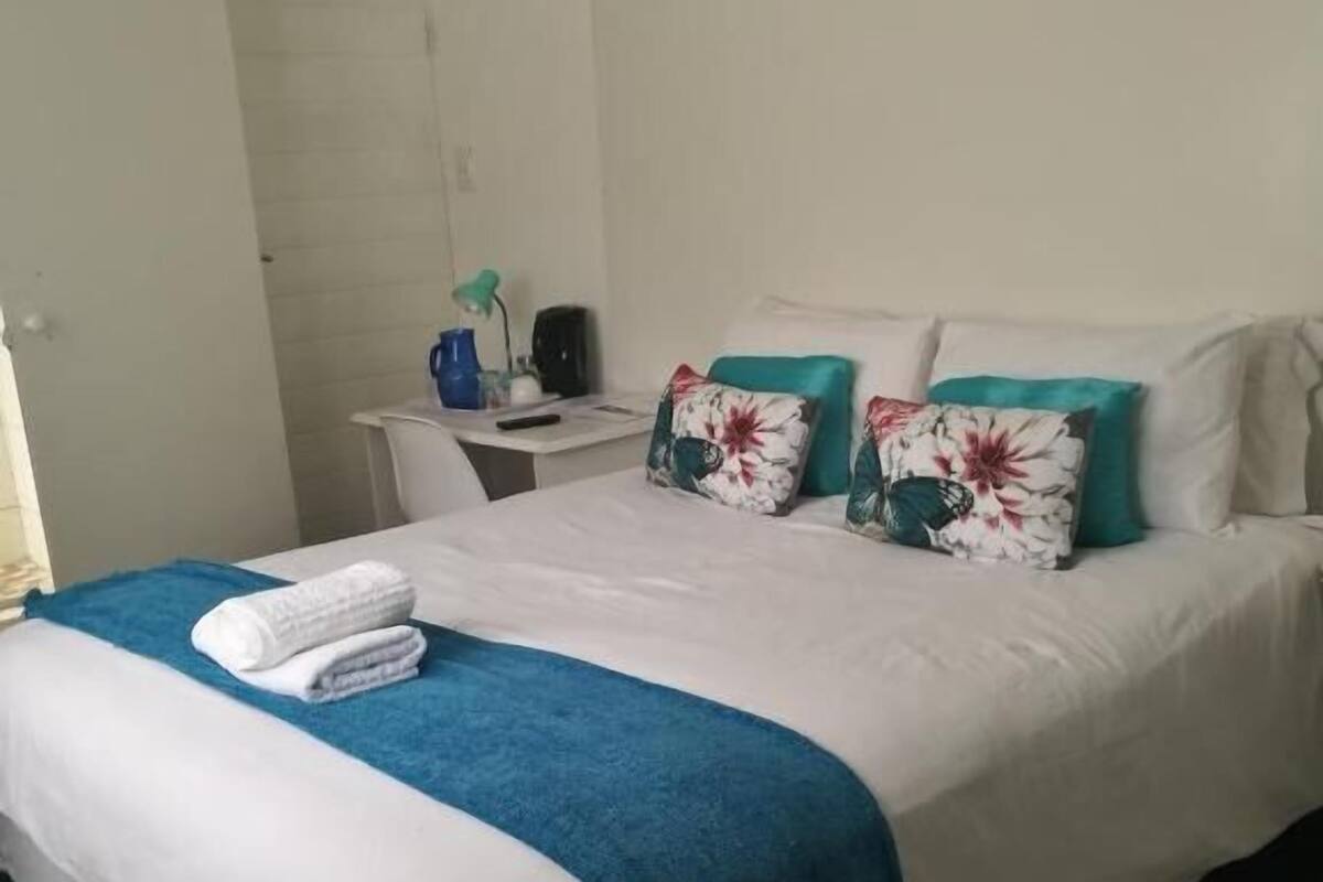 A neatly made bed with a blue and white bedspread, two floral pillows, and a pair of folded towels on the side.