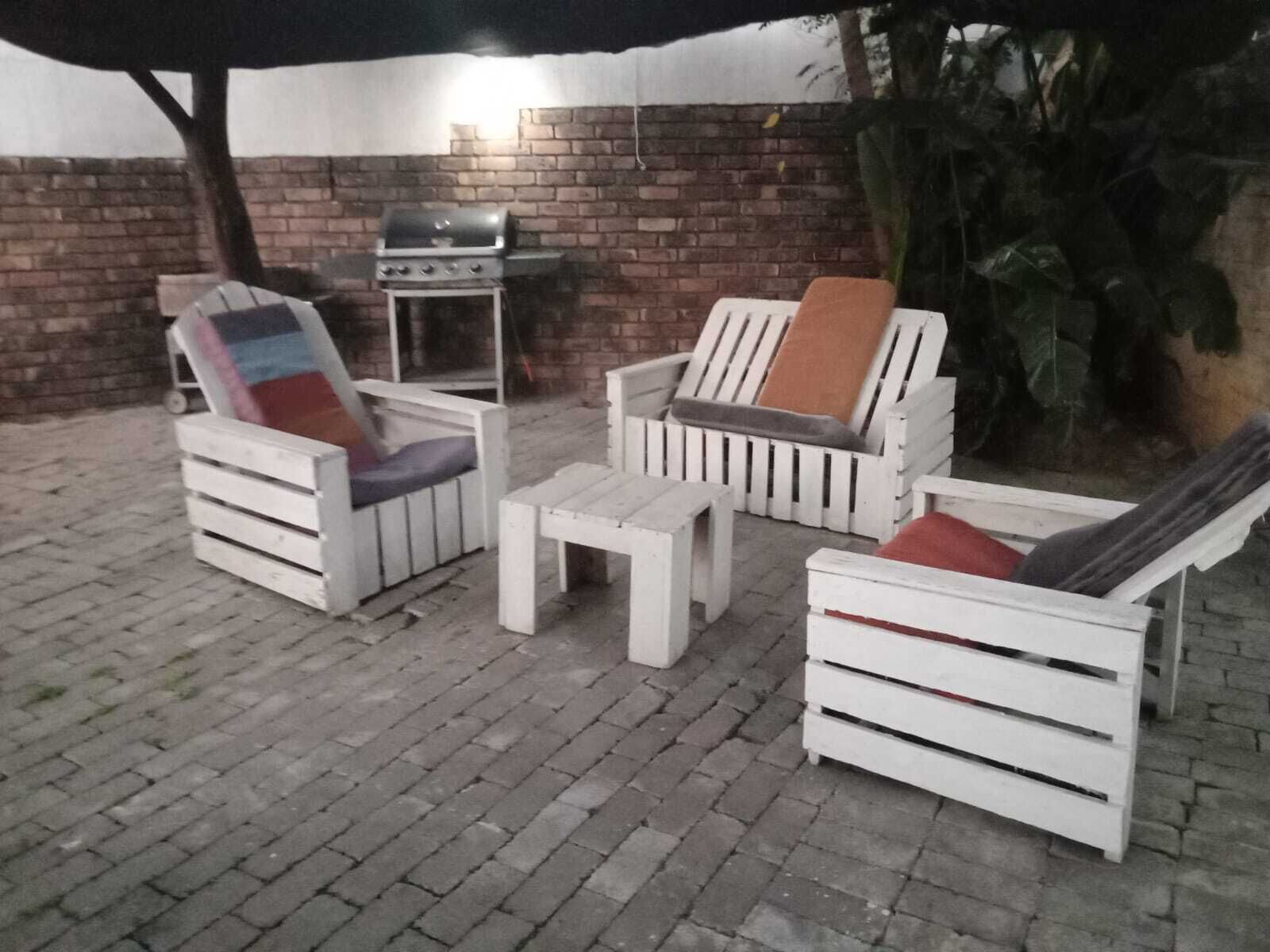 Terrassenmöbel im Freien, darunter weiße Stühle und ein Tisch, ein Grill und eine Ziegelwand.