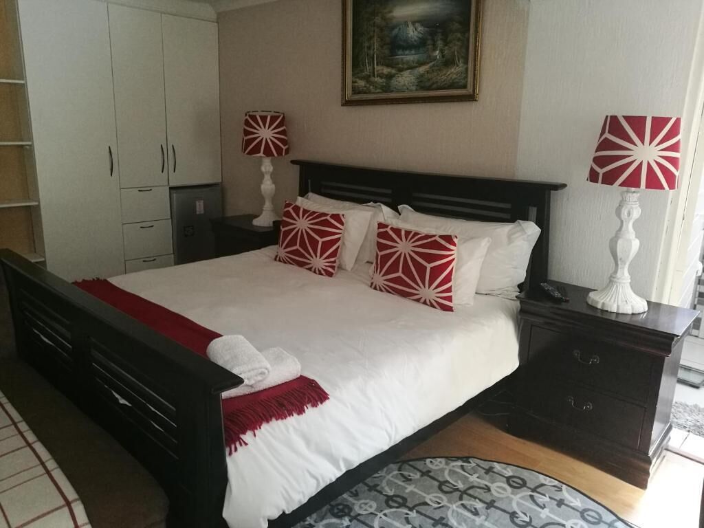 A neatly made bed with a white and red patterned bedspread, a dark headboard, and a white towel on the foot of the bed.