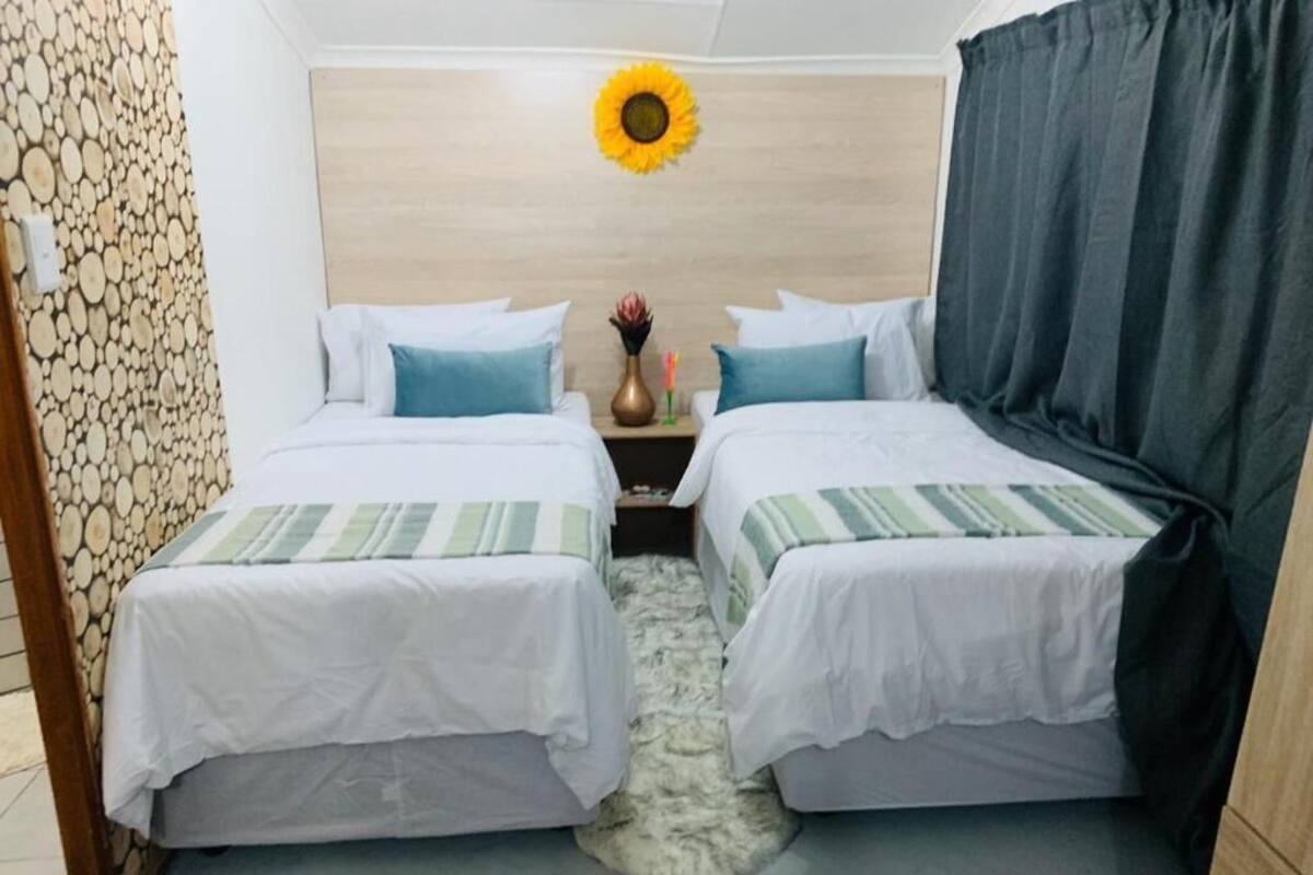 A room with two beds, a wooden headboard, a sunflower decoration, and a small table with a vase.