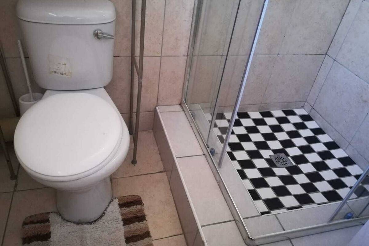 A bathroom with a toilet, a shower with a checkered floor, and a tiled wall.