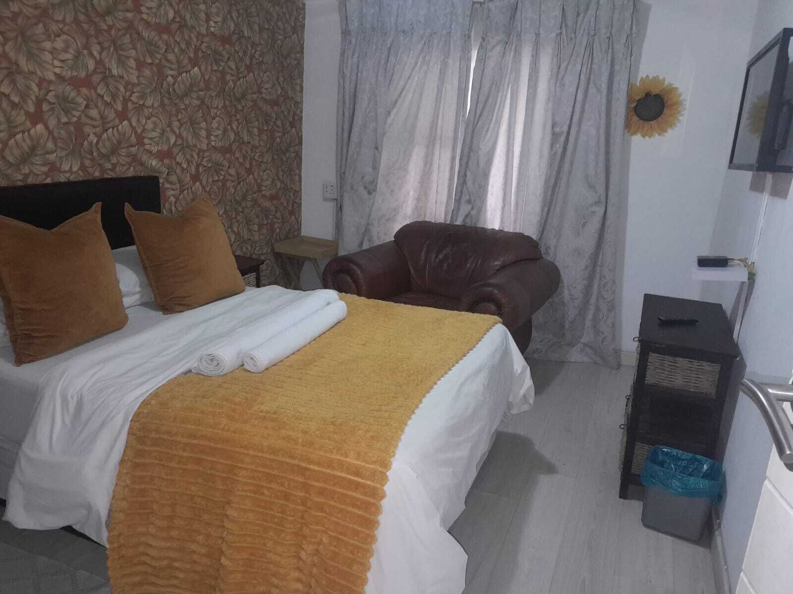 Une chambre d’hôtel avec un lit, un fauteuil en cuir marron, une petite table et un téléviseur fixé au mur.