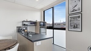 Une cuisine moderne avec un îlot central, une table à manger et des chaises. Des tableaux encadrés ornent le mur, et une grande fenêtre offre une vue sur l’extérieur.