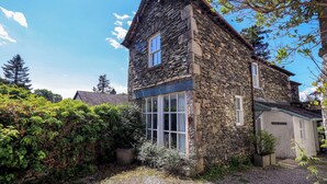 A stone cottage with a gravel driveway, surrounded by greenery. - Tower Cottage (Windermere)