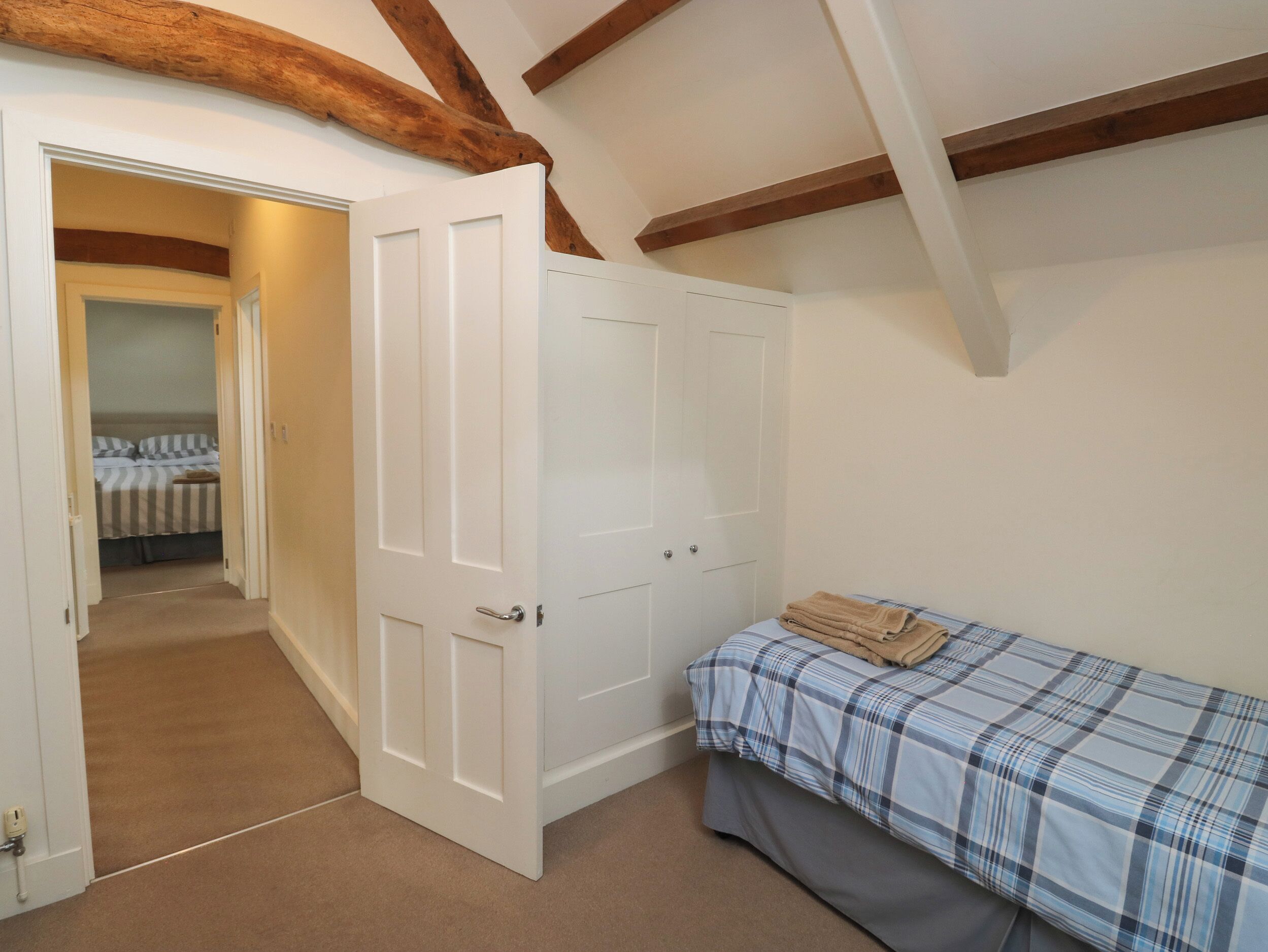 Un dormitorio con cama, una puerta que da a otra habitación y vigas de madera a la vista en el techo.