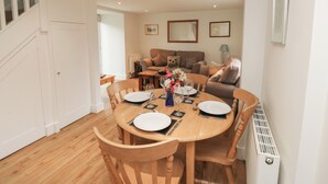 A dining area with a wooden table set for four, surrounded by chairs. There is a sofa and a radiator in the background. - Bantam Cottage (Honiton)