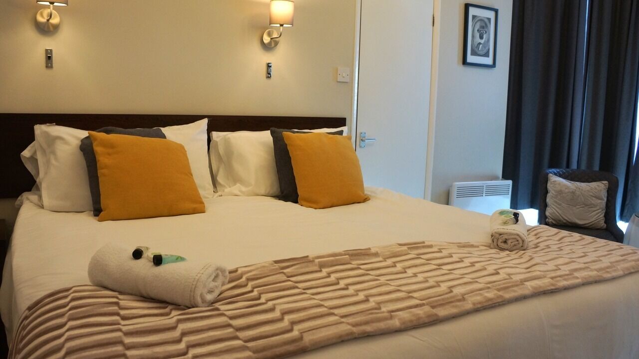 Une chambre d’hôtel avec un grand lit, deux lampes de chevet, un tableau encadré au mur et une fenêtre avec des rideaux.