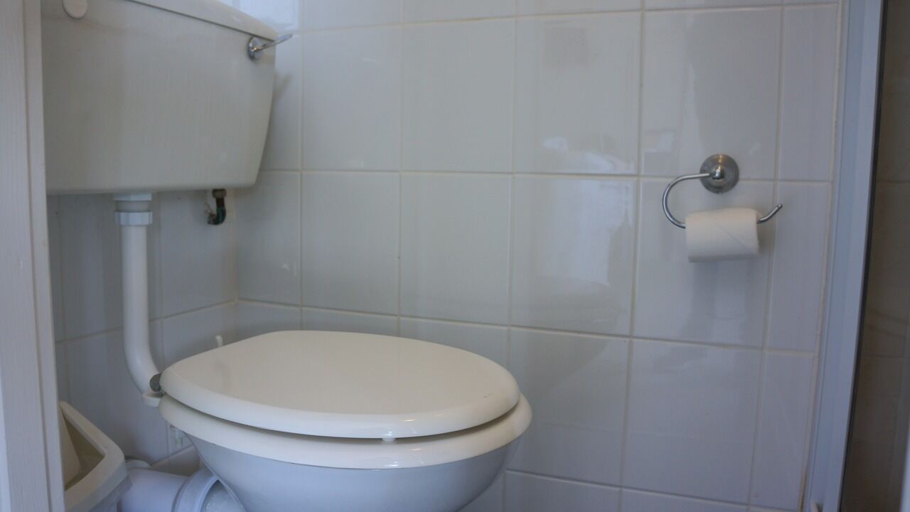 A standard white toilet with a tank, a toilet paper holder, and a visible pipe.
