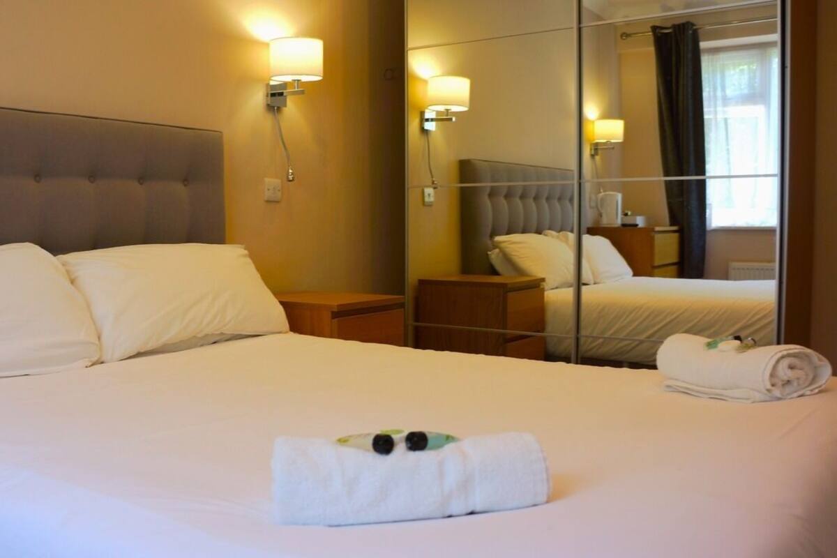 Une chambre d’hôtel avec un grand lit, une table de chevet, un miroir et une lampe fixée au mur.