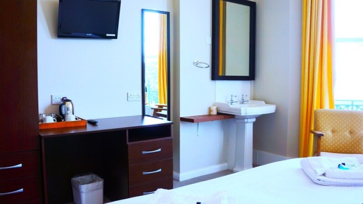 Habitación de hotel con cama, escritorio con silla, lavamanos y televisor montado en la pared.