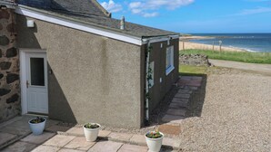 A coastal house with a stone facade, a gravel driveway, and a view of the sea. - Bella's Beach Cottage (Fraserburgh)