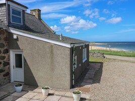 Una casa costera con fachada de piedra, camino de grava y vista al mar.