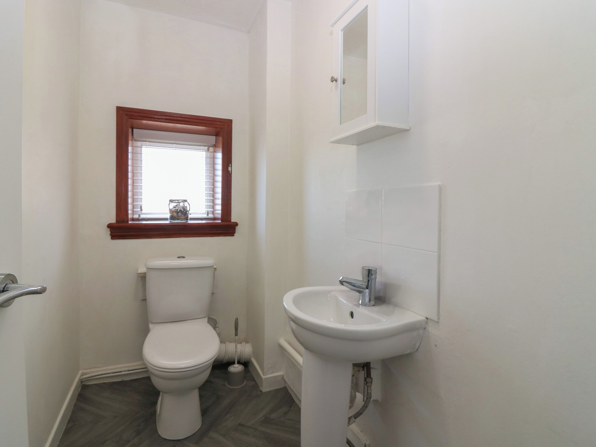 Een kleine, compacte badkamer met toilet, wastafel en een raam met zonwering.