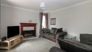 A living room with a fireplace, a sofa, a TV, and a coffee table. - Bella's Beach Cottage (Fraserburgh)