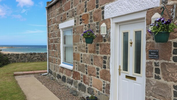 A stone building with a white door, a small window, and a sign reading "Bella's Beach Cottage". - Bella's Beach Cottage (Fraserburgh)