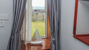 A room with a window, curtains, a small sailboat model, and a red-framed mirror. - Bella's Beach Cottage (Fraserburgh)