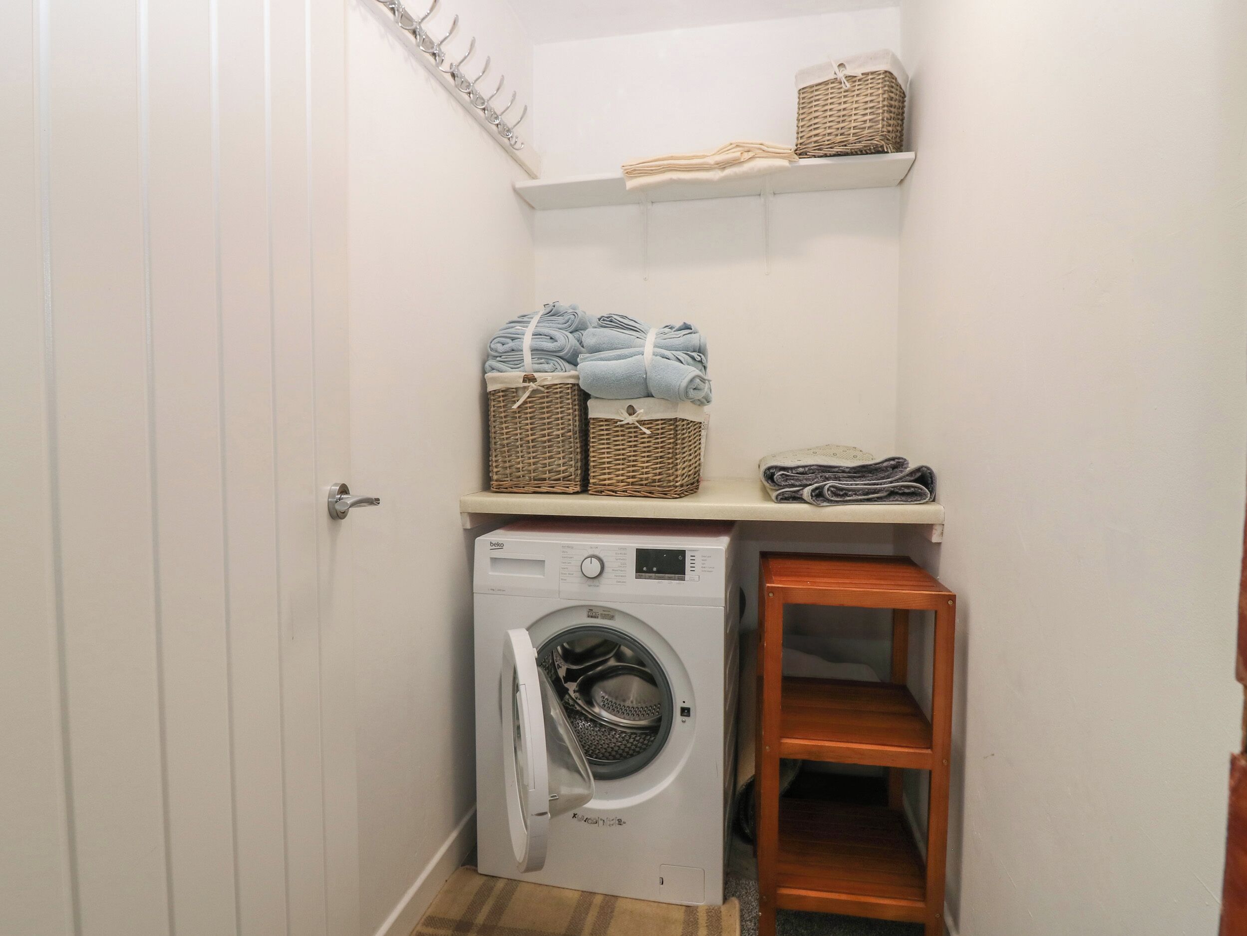 A laundry room with a washing machine, shelves with folded towels, and baskets.