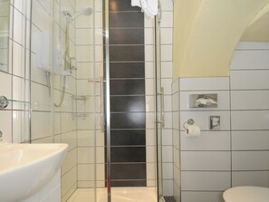A bathroom with a glass-enclosed shower, a white sink, and a toilet. - Sycamore Apartment (Lifton)
