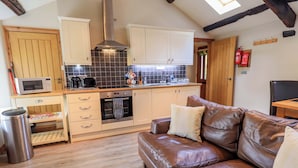 A compact kitchen with a microwave, toaster, and oven, a brown leather sofa, and a wooden floor. - Abbots Reading Mews 2 (Ulverston)