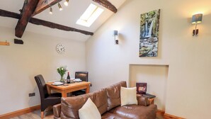 A cozy living room with a brown leather sofa, a wooden dining table, and a fireplace. - Abbots Reading Mews 2 (Ulverston)