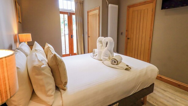 A hotel room with a large bed, a TV mounted on the wall, and a window with curtains. - Abbots Reading Mews 2 (Ulverston)