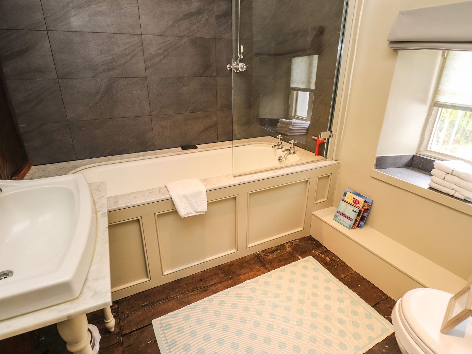 A bathroom with a bathtub, a sink, and a toilet. There is a window with towels hanging on the sill.