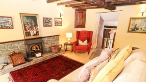 A cozy living room with a fireplace, a red armchair, a sofa with cushions, and a patterned rug. - The Farmhouse (Coniston)
