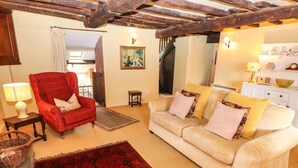 A cozy living room with a red armchair, a beige sofa with multiple cushions, a red patterned rug, and a wooden ceiling. - The Farmhouse (Coniston)